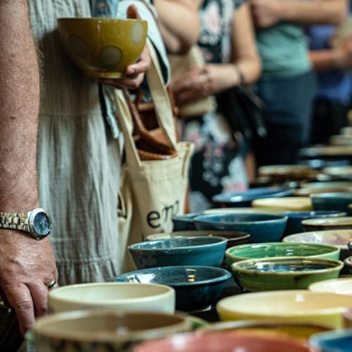 People lined up a table filled with bowls.