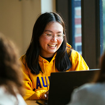 female student wearing yellow laurier hoodie smiling at her laptop