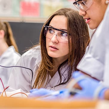 Student in a lab wearing safety glasses and a lab coat